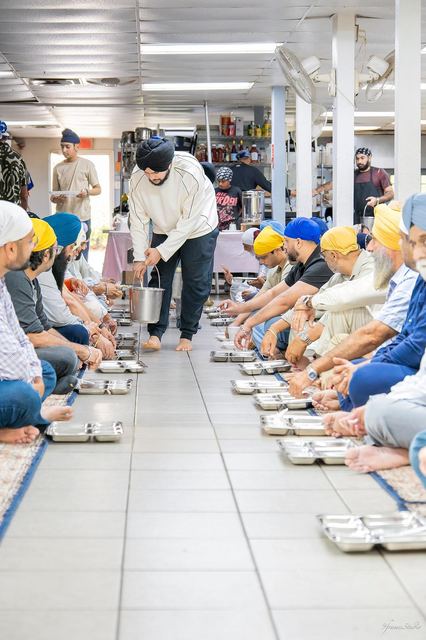 Sevadars serving langar to rows of Sangat seated on the floor